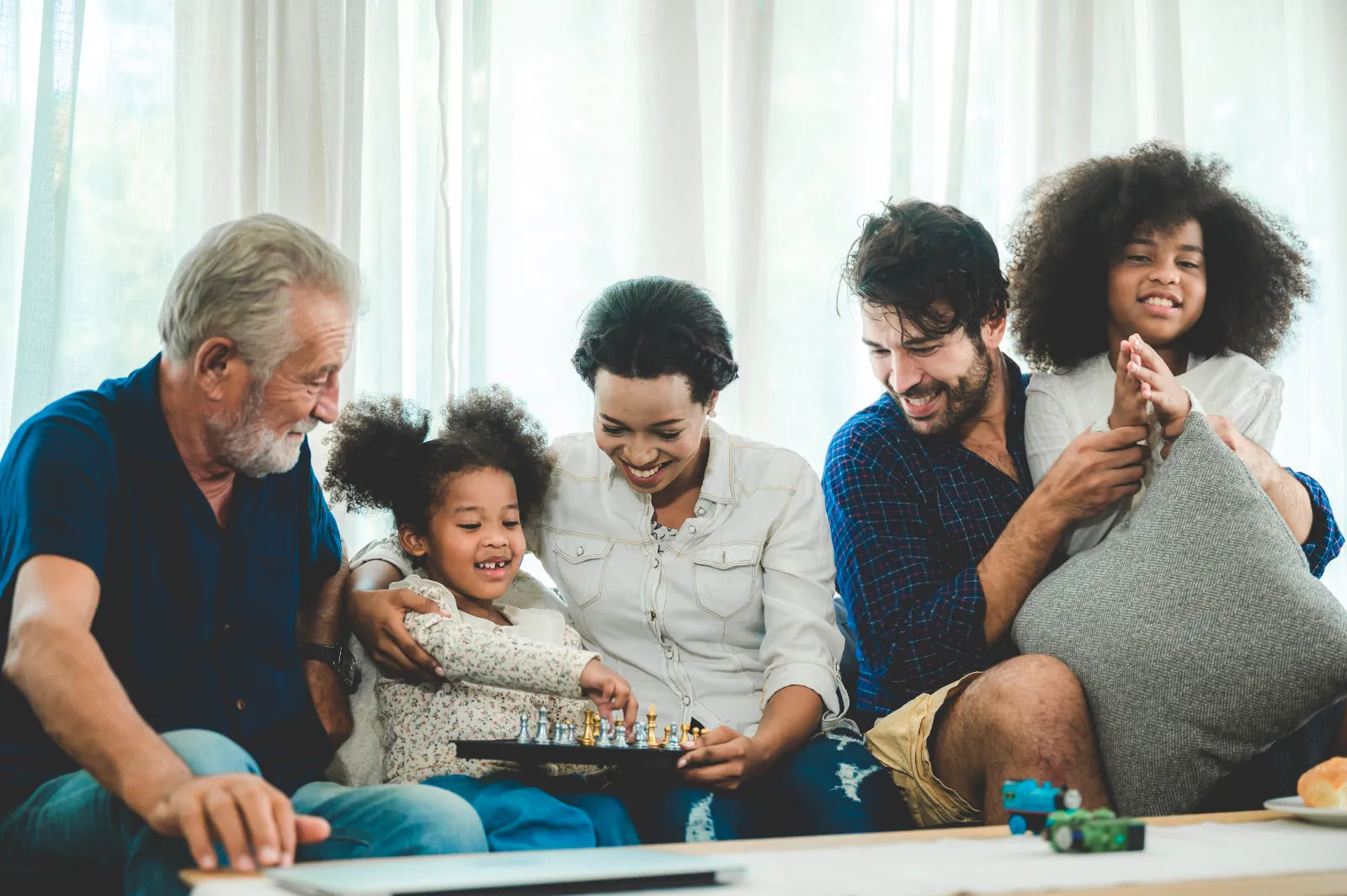Family playing chess together indoors, engaging in quality time with children and grandparents, highlighting the importance of connection and support in parenting.