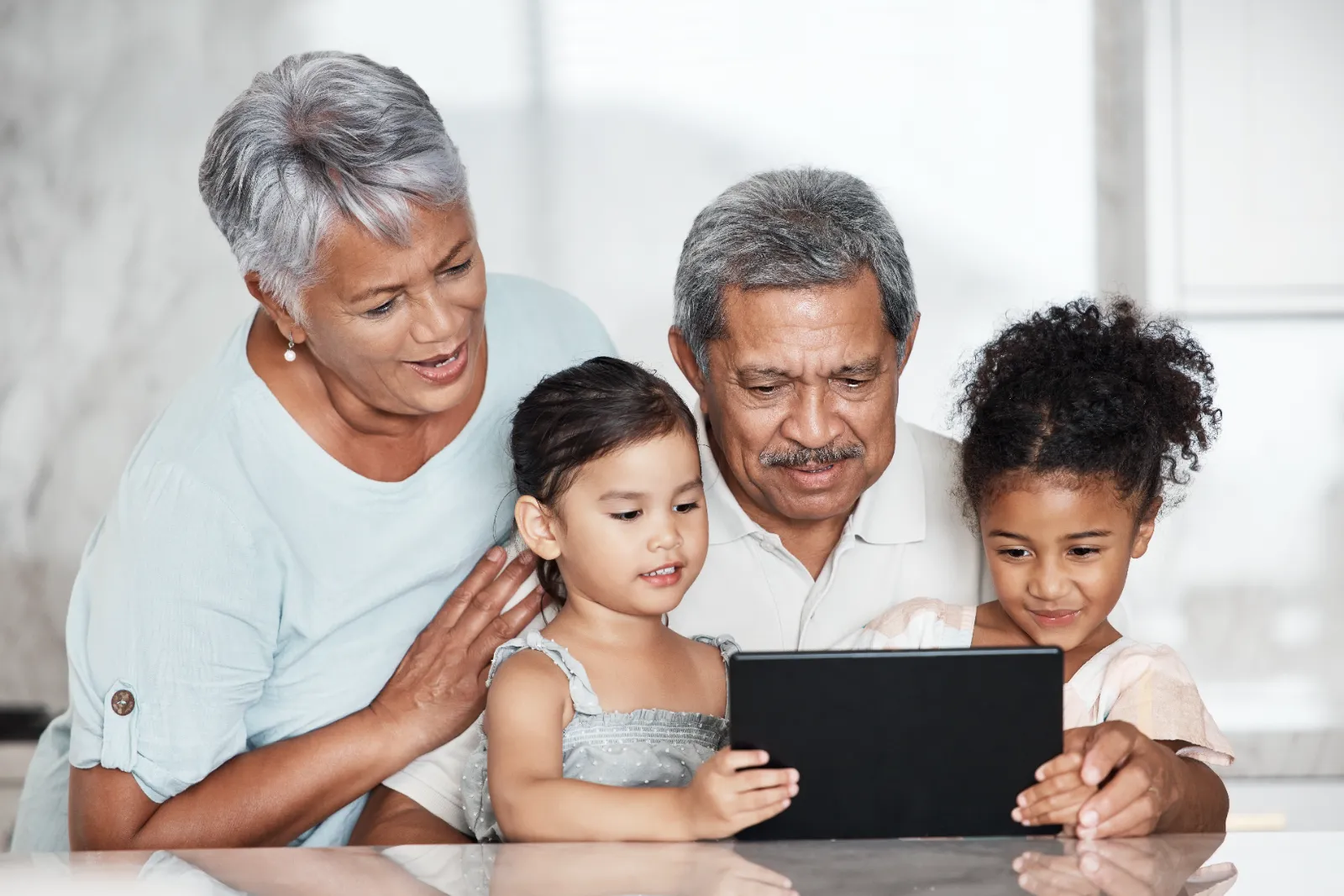 Grandparents and two young children engaging with a tablet, illustrating family interaction and screen time dynamics.