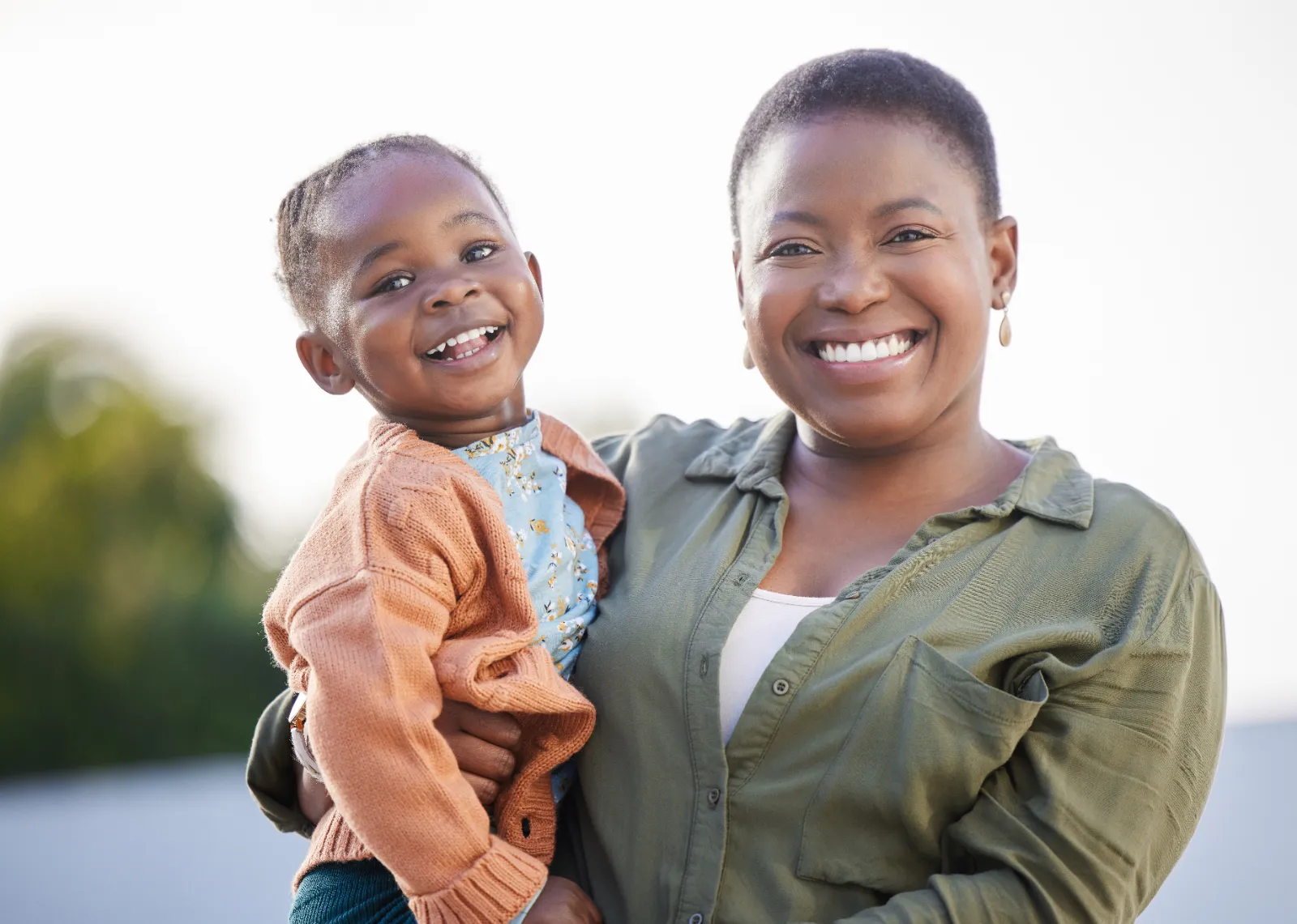 Smiling mother holding her happy child outdoors, representing the joy of single parenting and child safety in a supportive environment.